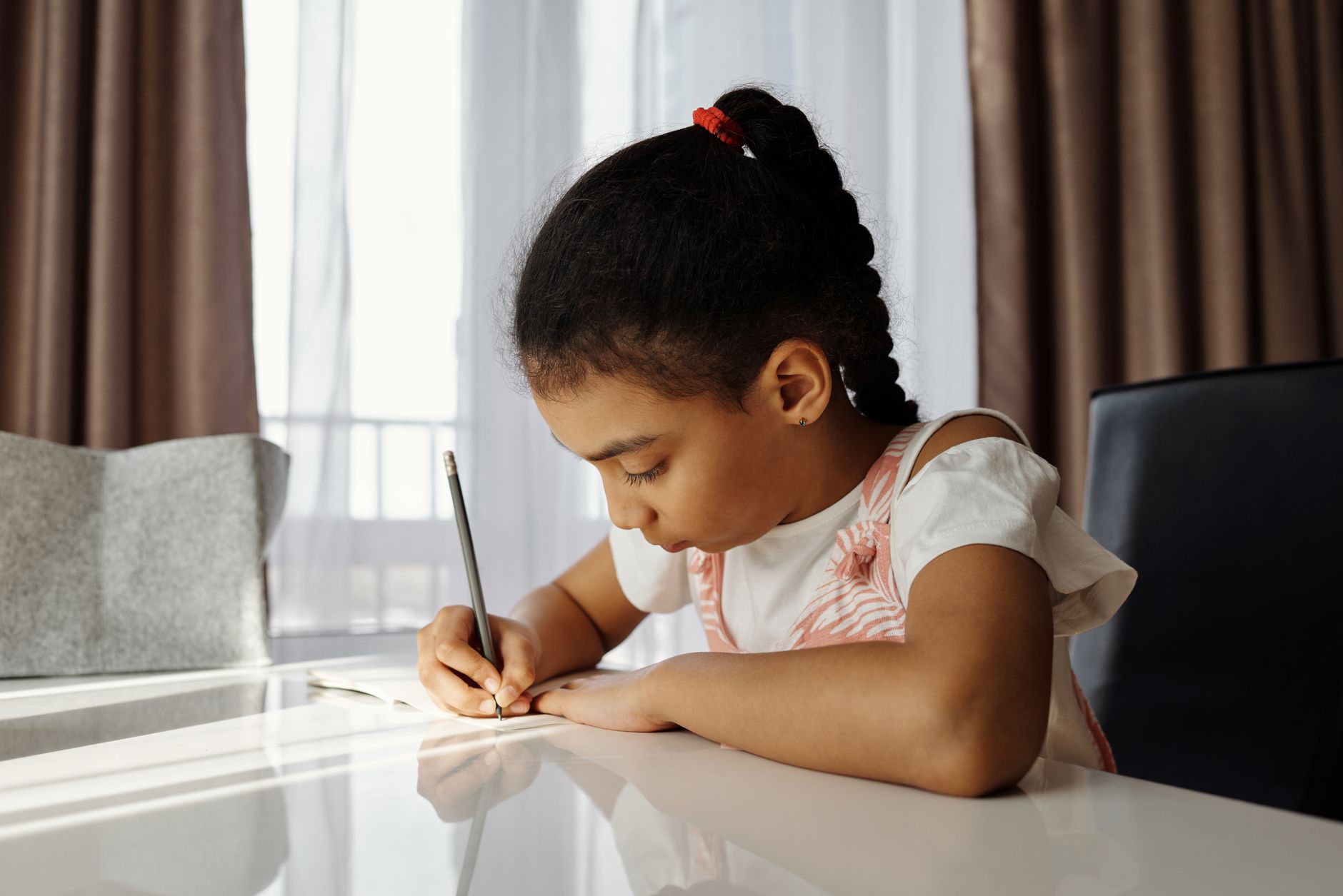 A child sitting at a desk, focused on writing in a notebook