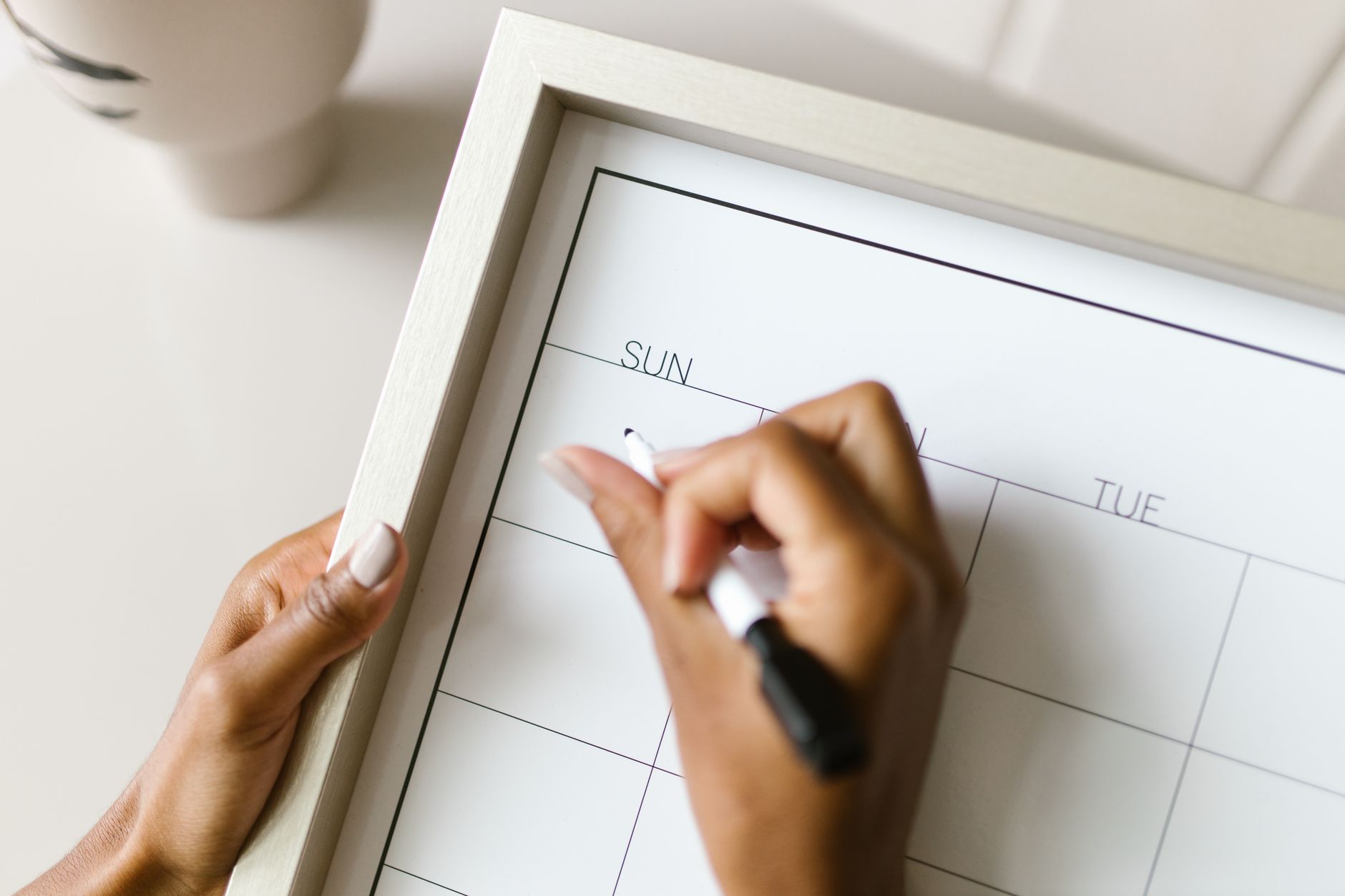 A hand writing on a shared weekly wall calendar labeled with the days of the week