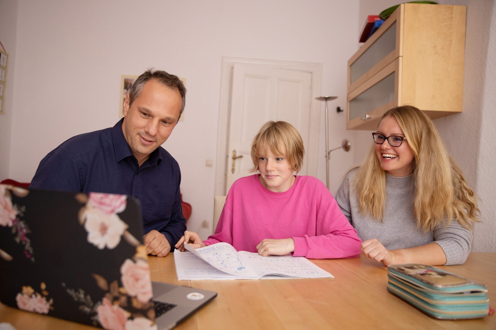 Two parents and their child looking over practice work together at a laptop on the kitchen table
