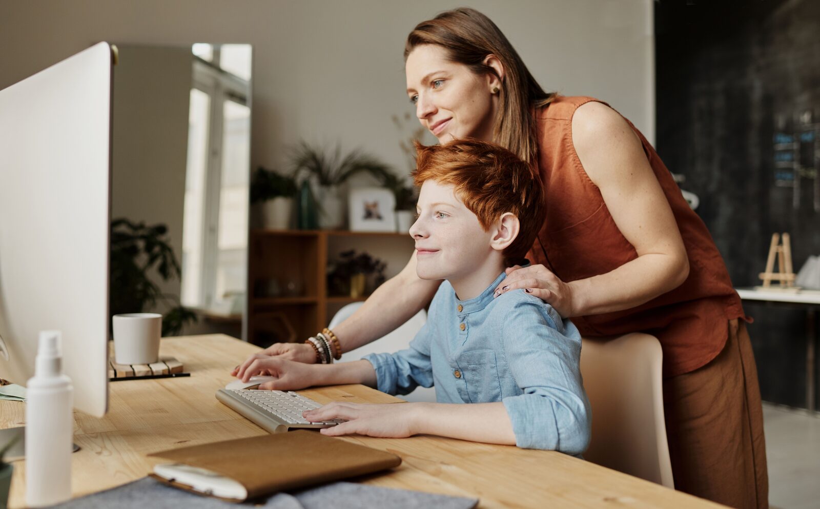 A parent and her son looking at a computer together at a desk at home