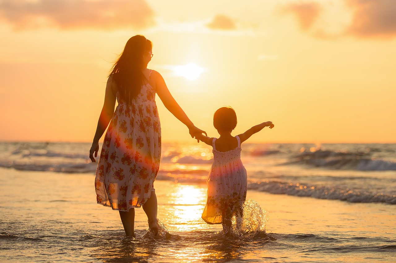 A parent and child walking by the water at sunset