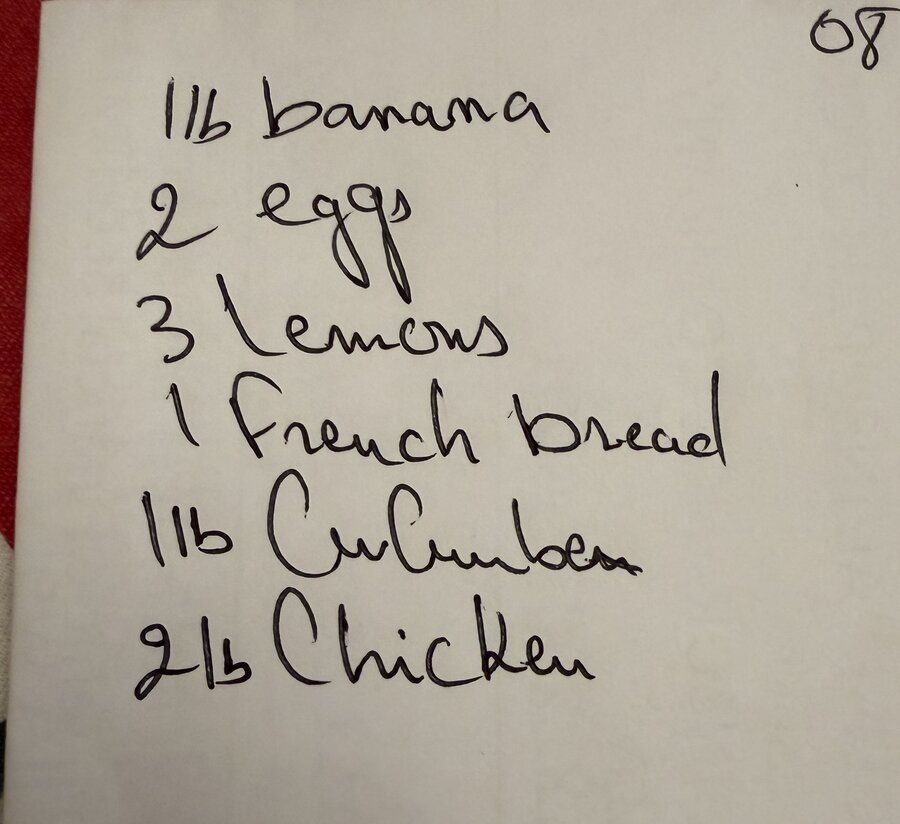 A handwritten grocery list on paper: 1lb banana, 2 eggs, 3 lemons, 1 French bread, 1lb cucumber, 2lb chicken